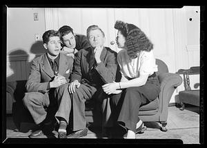 Woman and three men sit posing on couch