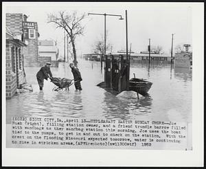 Unpleasant Easter Sunday Chore--Joe Rush (right), filling station owner, and a friend trundle barrow filled with sandbags as they sandbag station this morning. Joe uses the boat tied to the pumps, to get in and out to check on the station. With the crest on the flooding Missouri expected tomorrow, water is continuing to rise in stricken areas.