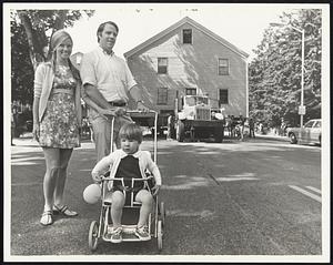 Proud Owners of old Clapp House, Mr. and Mrs. Charles H. Detwiller, 3d, of Brookline, with son, Chad, lead procession as house is moved along Washington street, Wellesley Hills, toward new site off Oakland street.