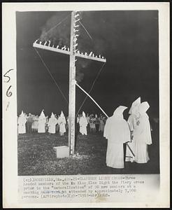 Klansmen Light Cross-Three hooded members of the Ku Klux Klan light the fiery cross prior to the “naturalization” of 90 new members at a meeting here tonight attended by approximately 7,000 persons.