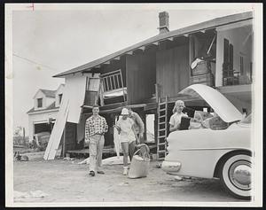 Moving Day-Vacationers at Swift Beach, Wareham, pack up and leave a summer cottage where walls were washed out, leaving the roof poised precariously. Left to right: Paul W. Carey of Brighton, Kendra Pitman of Attleboro, Philip J. Dobby at Brighton and Carol MacLeod of Chelsea.