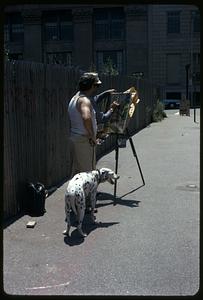 A man with a dog watching someone paint