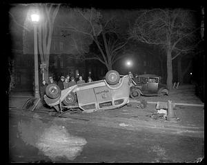 People stand behind an overturned automobile with "Longwood 5300" on its side