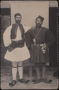 Two men wearing Greek costume stand posing together