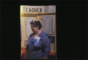 Woman wearing ribbon and NEA name tag standing by "Teacher" sign