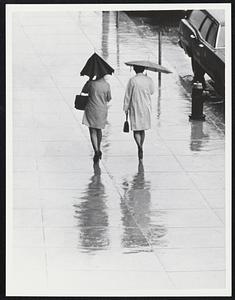 Two women walking in the rain holding umbrellas