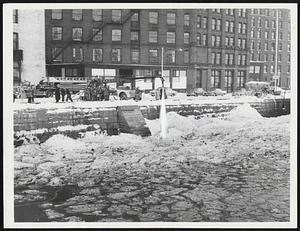 Boston Iceberg, caused by the dumping of snow removed from city streets, become formidable problem for firefighters and Coast Guardsmen yesterday in the Fort Point Channel. The dumped snow congealed into icy mass endangering pilings and the passage of fire boats up the channel. Stream of water from fire department fire truck on Dorchester avenue is trying to break free.