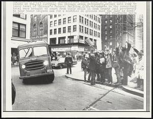 Demonstrators raise their arms in clenched fist salute as van, (L) carrying the Chicago Seven defendants, swings into ramp to lower level of Chicago's Federal Building 2/18. Defendants in the conspiracy trial were brought to court from their cells in Cook Country jail presumably to hear their lawyers ask for a mistrial on grounds that the jury is deadlocked.