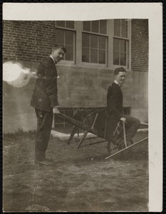 Two young men with wheelbarrow, rake