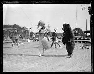 A woman in costume holds the leash of a bear on roller skates