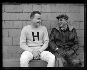 A member of Harvard crew sitting with an unidentified man wearing a coat and gloves