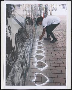 Young person spray painting white heart outlines on the street
