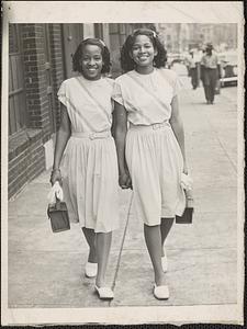Two young women walk down a sidewalk