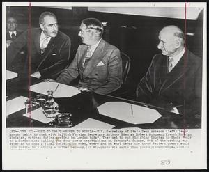 Meet to Draft Answer to Russia-- U.S. Secretary of State Dean Acheson (left) leans across table to chat with British Foreign Secretary Anthony Eden as Robert Schuman, French Foreign Minister, watches during meeting in London today. They met to put finishing touches to their reply to a Soviet note calling for four-power negotiations on Germany's future. Out of the meeting was expected to come a final decision on when, where and on what terms the three Western powers would join Russia in planning a united Germany.