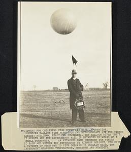 Equipment for obtaining high upper air mass information. Sounding balloon, with parachute and meteograph (in whisker basket) attached, ready for releasing. The balloon rises until it bursts and the instruments fall is retarded by means of a small parachute. an attached card requests the finder to pack and return the instrument by express (collect) for which a payment of from one to five dollars is usually made. Instrument measures temperature, pressure and humidity.