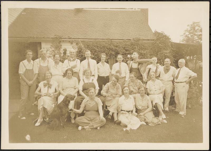 Group of men and women posed in front of a garage or house