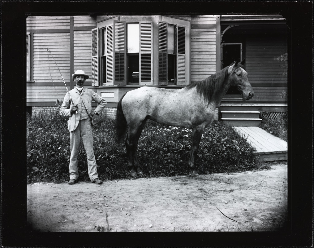 Man with a gray horse and a whip in front of a house