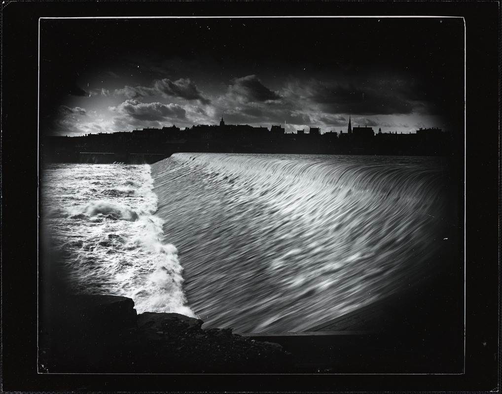 Time-lapse image of water flowing over the dam, with Holyoke skyline in the background