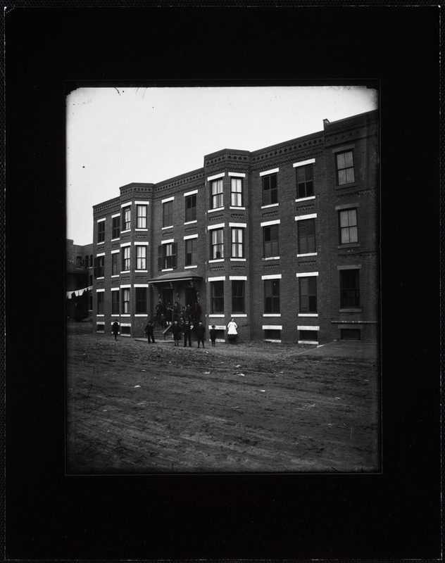 A large group of boys in hats and jackets standing on the steps of an apartment building on Newton Street