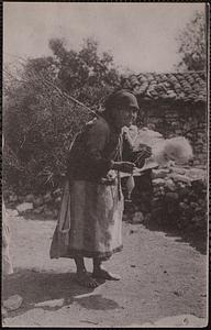 An old woman spinning using a spindle with branches on her back