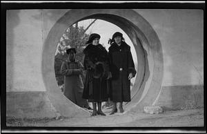 Two women in a circular opening, with someone in the background