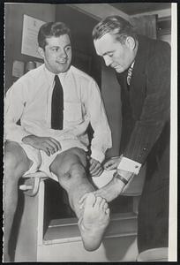 Fireball Frankie Sinkwich's Knee under observation by Dr. Mal Stevens (right). Sinkwich saw little action as a member of the New York (football) Yankees during the 1946 season while Stevens has just been signed by the club as team physician.