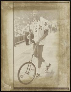 Bill Russell of the Boston Celtics pushes a unicycle off the Boston Garden floor after it was presented to him by the Charles Unicycle of New York City. Russell preferred to push the unicycle off rather than try to ride it.