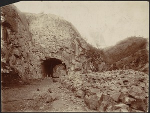 Arched tunnel through side of mountain, two men standing inside