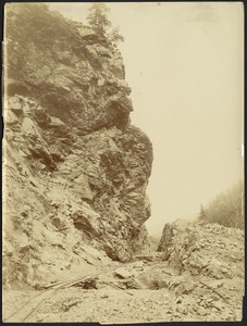 Railroad track construction through mountain crevice, carts in distance