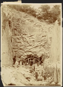 Construction of tunnel through mountain, men standing on rail tracks