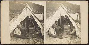 Five men inside of a tent, one speaking into a cylinder phonograph