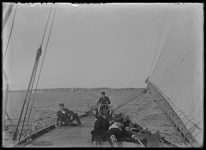 View of man at helm of sailboat, people seated in background