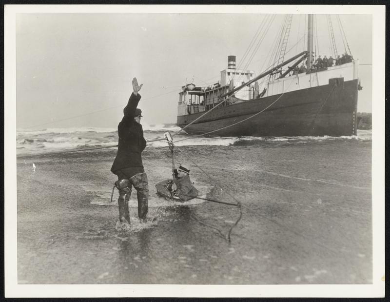 Rescued by Breeches Buoy After 18 hours of work in an effort to save the cargo, the Steamer Schooner Tiverton was finally abandoned by its caption, Adolph Ahlin, and crew, off Eureka, Calif., where it ran aground early on January 20. All members of the crew were landed via the breeches buoy, and the above scene shows John McCann, oiler, the first of the crew to be rescued, in the carrier. Other members of the crew can be seen grouped on the forepeak of the grounded ship.