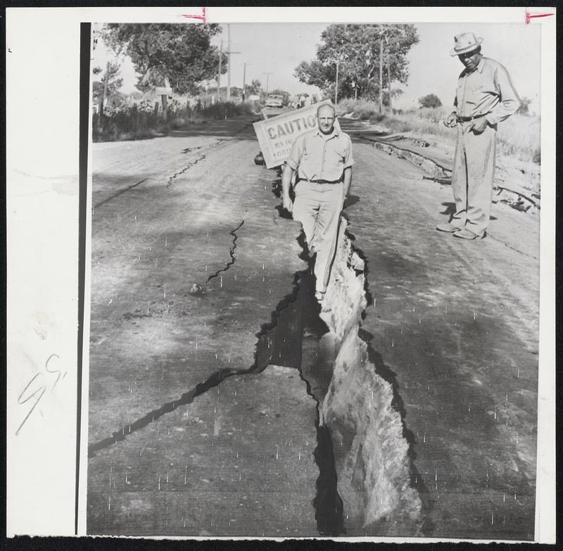 Nevada Earthquake Cracks Road -- Large cracks in road make driving hazardous in Nevada's Churchill County. The cracks were opened by Monday night's heavy quake which shook northern Nevada. Highway worker stands in crack after setting up caution sign for motorists.