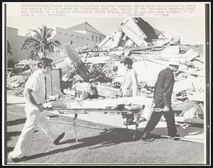 An injured patient (Note: face was covered to keep the debris off) is rushed by stretcher past the rubble of the Veteran's Hospital that was leveled by a massive earthquake early 2/9. At least 26 persons were killed, 11 of them at this hospital.