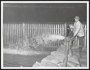 Needham town employe Joseph Conner stands by pump on top of sandbags rear of Dr, Gordon's House on Edgewater Drive. Conner says this spot is almost 300 ft. from normal bank of Charles River. He also said there was about 1500 sandbags place out near this spot.