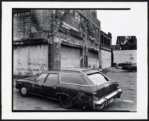 Car parked in front of graffitied building