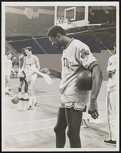 Bill Russell reads a piece of paper while holding a basketball on the court
