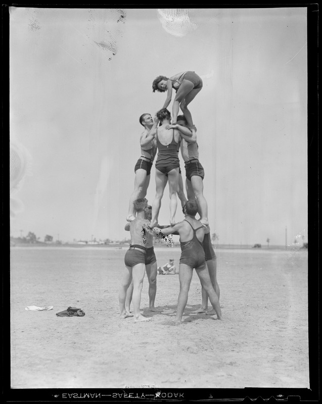 Strongmen at the beach build pyramid with girl at top