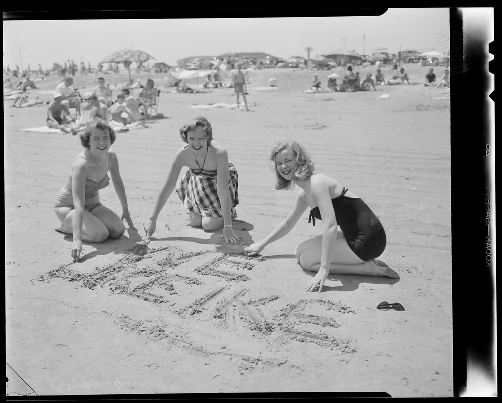 Three beautiful beachgoers write "We like Ike" in the sand