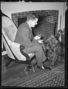 Unident. man with dog in front of fireplace