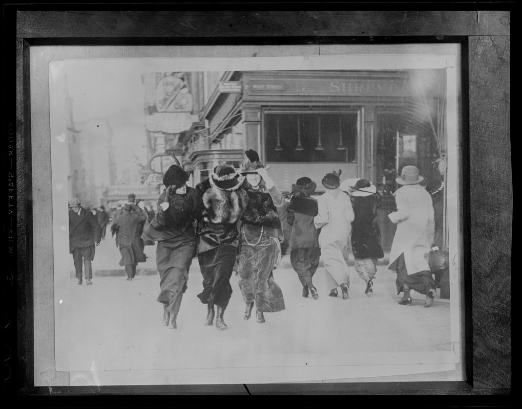 Stylish belles in floppy hats and long velvet skirts on a windy day, corner of Tremont & West Streets