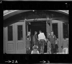 Men standing on either side of doorway, including Headmaster Joseph Malone, far left, at English High School while students enter, most likely during student demonstrations