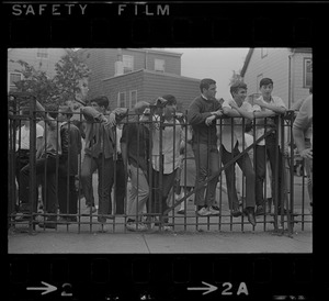 Group of young men leaning against gates in front of East Boston High School
