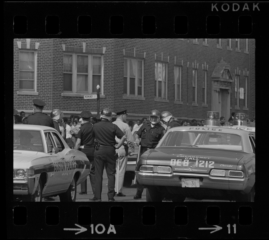 Riot police standing among cars on Washington Street near Jeremiah E. Burke High School after unrest broke out during student demonstrations