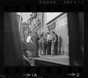 Police standing outside of a patrol car and speaking with a group of young Black men on the sidewalk, most likely after unrest broke out during student demonstrations