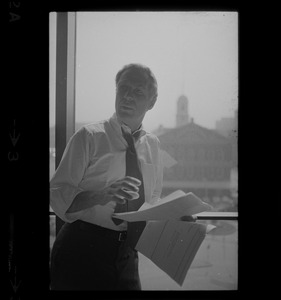 Mayor White standing by a window in his City Hall office overlooking Faneuil Hall and reviewing papers