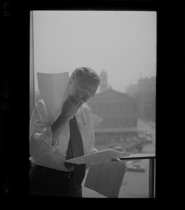 Mayor White standing by a window in his City Hall office overlooking Faneuil Hall and reviewing papers