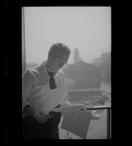 Mayor White standing by a window in his City Hall office overlooking Faneuil Hall and reviewing papers