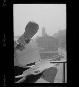 Mayor White standing by a window in his City Hall office overlooking Faneuil Hall and reviewing papers